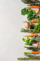 Variety of fresh kitchen herbs with mini carrots and champignon mushrooms in row over white marble background. Flat lay, space. Cooking concept, food background.