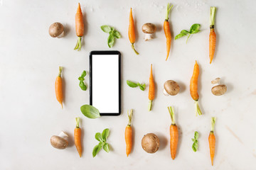 Fresh basil herbs with young mini carrots and champignon mushrooms in rows, smartphone white screen over white marble background. Flat lay, space. Cooking concept, food background.