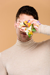 man with alstroemeria flowers on hand covering face isolated on beige