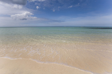 white beach with crystal clear water little waves blue sky and white clouds,  a tranquil relaxing scene on a hot sunny day