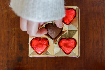 Woman's hand taking a chocolate heart candy from chocolate box