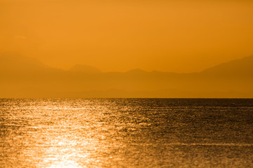 sunshine sun reflection in the ocean sea water with mountain silhouettes in the background, a tranquil summer sunset holiday mood