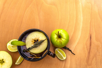 Fruit tea concept. Fresh lime and apple, dry herbs. Glass brown cup on a wooden background, top view