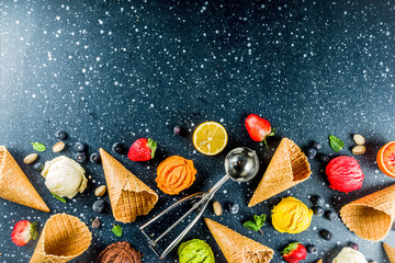 Colorful fruit and berry, nut, chocolate and vanilla ice cream, with waffle ice-cream cones, with fresh fruit and berries, top view copy space dark blue background