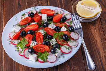 plate of salad with red tomato, green pepper and greek cheese on a wooden table