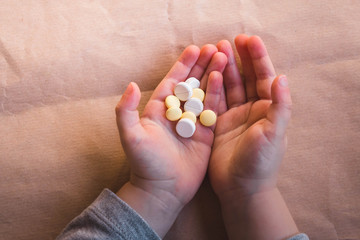 Baby hands with pills on paper background. Sick Child Has Medicine and Vitamins, Closeup, Neutral Background