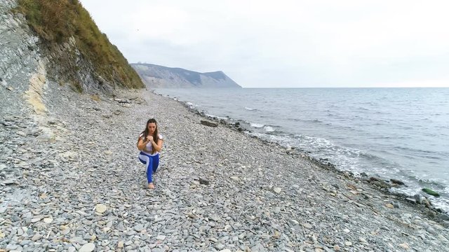 Girl doing squat lunge the bodyflex during breathing exercises on the rock and sea background.