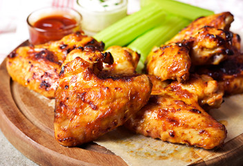 Delicious chicken wings on a wooden cutting board. Close-up shot of tasty chicken wings with perennial celery, sour cream dip and bbq sauce.