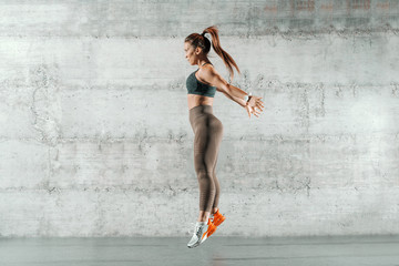 Caucasian sporty woman dressed in sportswear and with ponytail jumping. In background wall.