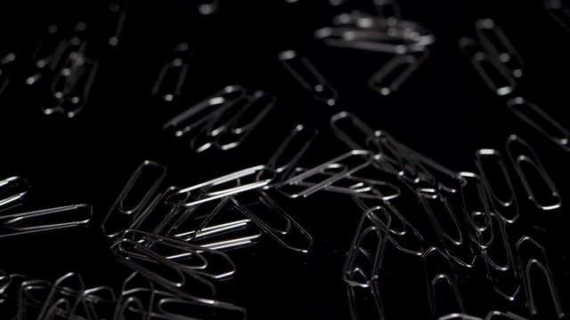 Macro slide shot over paper clips, more paper clips falling down in slow motion.
