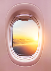 Airplane interior with window view of sunset above clouds.