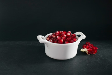 Organic fresh pomegranate seeds in white bowl on the black stone plate.