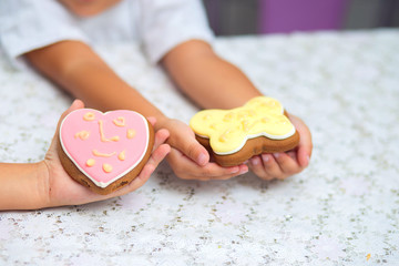 Pink Cookies in the form of a butterfly and heart lie on a children's hand. The child decorated cookies with cream independently. Children's drawing