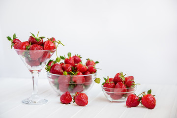Red ripe strawberries in a glass bowl on a white wooden table. Harvest from your garden.