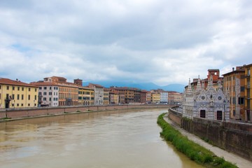 Fototapeta premium The Arno River and the small Gothic church of Santa Maria della Spina on the waterfront of Pisa. Cloudy, rainy weather. Pisa, Italy.