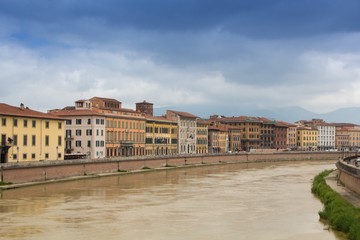 Old colorful buildings along the Arno river. Pisa cityscape. Embankment of the Arno river in Pisa. Gloomy rainy and cloudy day. Pisa, Italy.