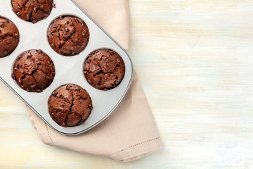 An overhead photo of chocolate muffins in a pan, shot from the top on a light background with copy space