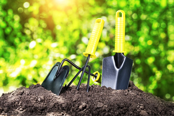Garden tools rake shovel and chopper on pile of earth under bright sun