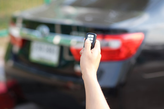 The focus image of the hands of people who are pressing on the remote car key has a blur background image of a car in the morning in Bangkok, Thailand.