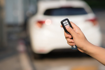 The focus image of the hands of people who are pressing on the remote car key has a blur background image of a car in the morning in Bangkok, Thailand.