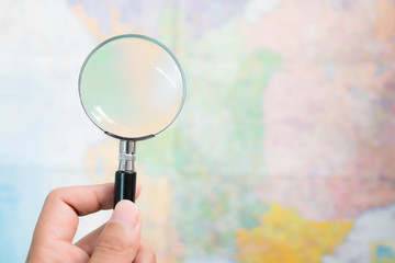 Focus on the hand holding a black magnifying glass with a blurred background of the map.