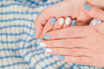 Closeup top view of female fingers with two colors manicure of blue and white colours. Hands of young woman isolated on cozy warm blanket. Horizontal photography.