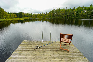 Fishing equipment on seat on lake. Feeder carp rods on wooden pier.