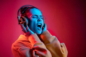 Gordijnen Fashion pretty woman with headphones listening to music over red neon background at studio. © master1305