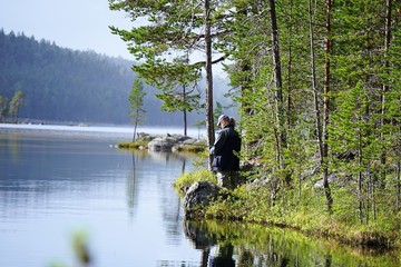 Fototapeta na wymiar Man fishing, casting a fishing rod, in the lake in Lapland, Finland. Calm water, lake surrounded by trees. 