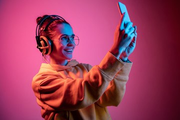 Fashion pretty woman with headphones listening to music and making selfie photo over red neon...
