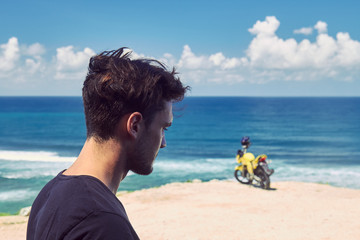 Fototapeta premium Young handsome man standing near motorcycle on the tropical beach.