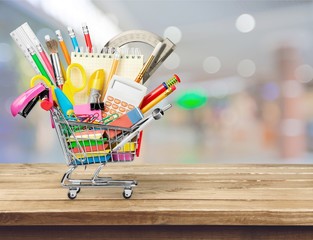 Variety office supplies in little shopping cart on wooden table  on background