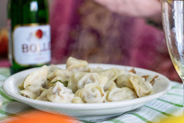 Plate of hot dumplings with steam and glass of champagne at background on the table on holiday