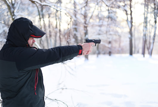 A man with a gun in his hands is aiming in the winter forest.