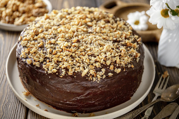 Homemade chocolate cake covered with chocolate icing and sprinkled with walnuts