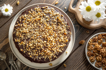 Homemade chocolate cake covered with chocolate icing and sprinkled with walnuts