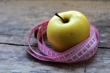 Beautiful yellow apple and centimeter ribbon on wooden background.