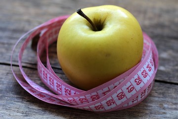Beautiful yellow apple and centimeter ribbon on wooden background.