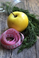 Beautiful yellow apple and centimeter ribbon, as well as branches of green dill in a glass jar on a wooden background.