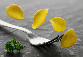 Falling pasta, macaroni and fork closeup on textural stone background.