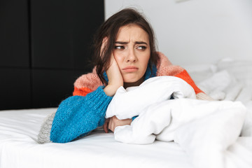 Photo of upset woman 20s wearing sweater, lying in bed at home