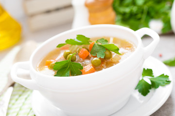 Summer light vegetarian vegetable soup with carrot, potato, cabbage and grean peas on white background. Diet healthy and tasty lunch. Baby food