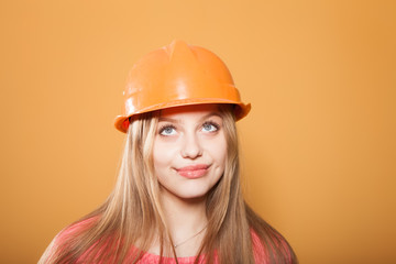 Beautiful emotional girl in the construction helmet on an orange background