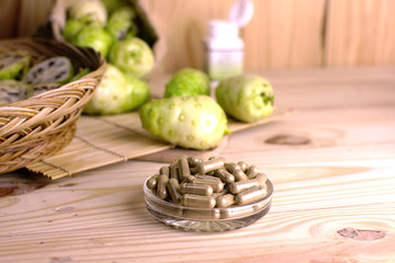 Noni powder capsule in glass dish with noni fruit and noni slice