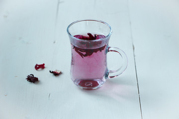 Red carcade tea in transparent glass cup at white wooden background, simple and nice drink picture for calm and peaceful rest time illustration.