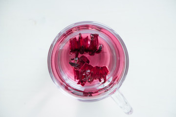 Red carcade tea in transparent glass cup at white wooden background, simple and nice drink picture for calm and peaceful rest time illustration.