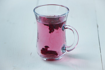 Red carcade tea in transparent glass cup at white wooden background, simple and nice drink picture for calm and peaceful rest time illustration.