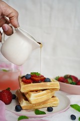 Male hand pouring maple syrup on stacked waffles, selective focus