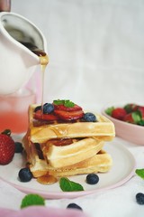 Male hand pouring maple syrup on stacked waffles, selective focus
