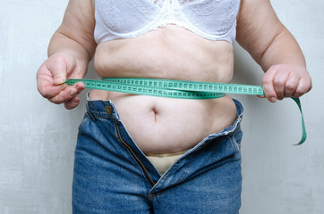 Woman with huge belly, get upset and tightening the measure tape on her waist.Concept of unhealthy eating